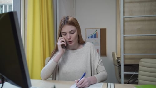 Woman Talking on Phone and Writing at Desk