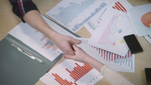 Successful Handshake Over Financial Charts in Office