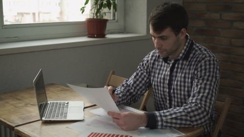 A Man Looks At The Table And Makes a Note In Notebook.