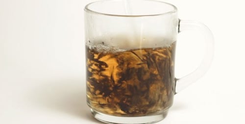 Pouring Water Into A Glass Mug With Tea Leaves