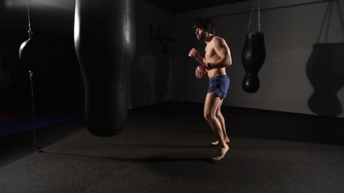 Muscular Handsome Fighter Giving a Forceful Forward Kick During a Practise Round With a Boxing Bag.