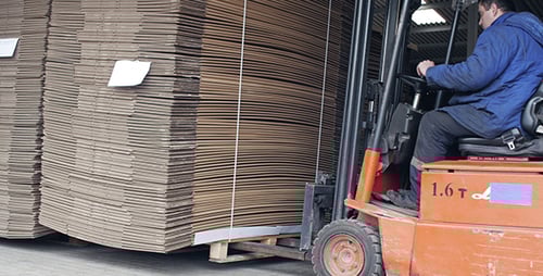 Forklift Moving Stack of Cardboard in Warehouse