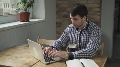 Man Works at Laptop with Coffee and Notebook