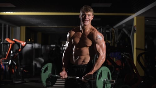 Overcoming Young Adult Bodybuilder Doing Weight Lifting In Gym.