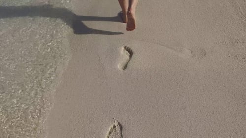 Female Feet Walking On Sandy Beach With Footprints