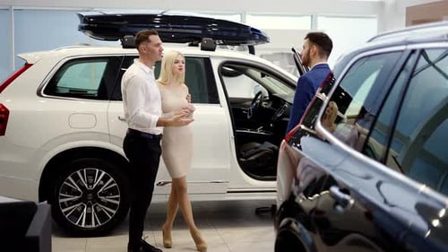 Couple Talking to Car Dealer in Dealership Discussing Automobiles Looking at Luxurious New White