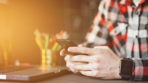 Junger Mann, der von zu Hause aus mit Smartphone und Notebook arbeitet.