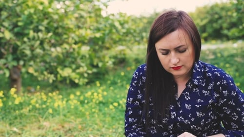 Attractive Woman Reading Book In Park Looking At Camera And Smiling.