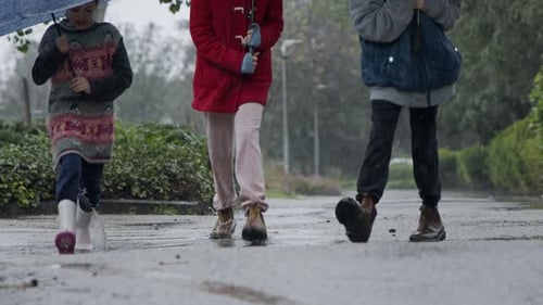 Three kids running happy in the rain and puddles with umbrellas