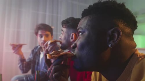 Three Multiethnic Guys Friends Eating Delivered Fresh Pizza Watching Tv Together at Home in Evening