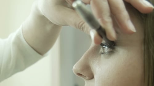 Artista de maquillaje que aplica delineador de ojos en el párpado.