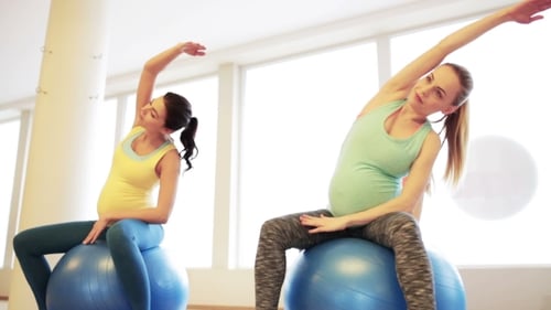 Glückliche schwangere Frauen, die im Fitnessstudio auf Fitball trainieren