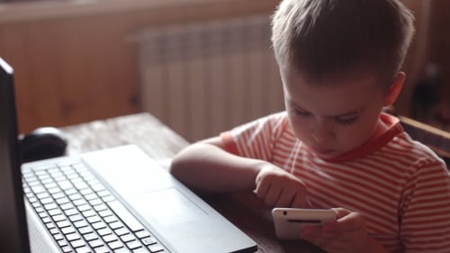 Young Boy Using Smartphone at Desk With Laptop