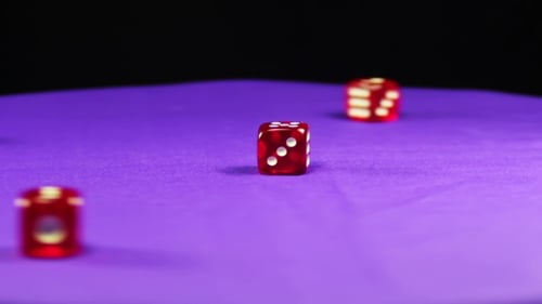 Red Dice Rolling on Purple Felt Surface