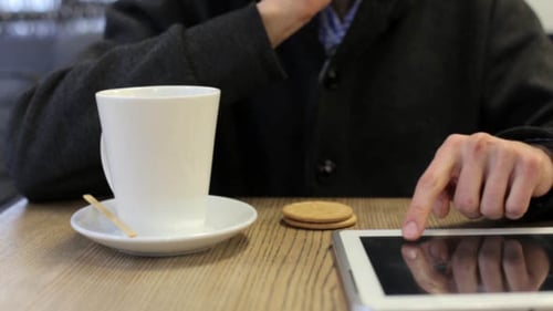 Mann in einem Café trinkt Tee und arbeitet mit Tablet