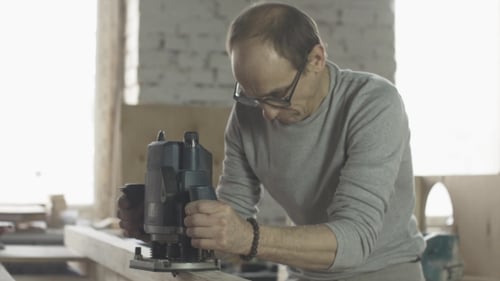 Man Using Wood Router on Plank in Workshop