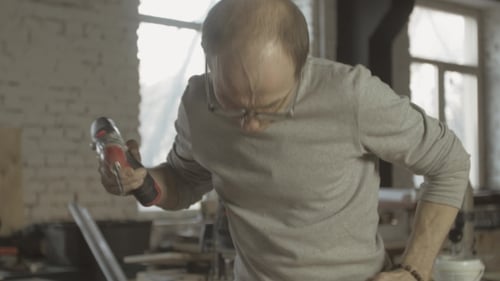 Man Drills Wood in Workshop with Power Drill