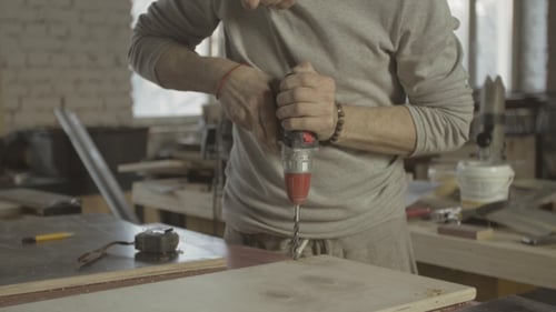 Man Drilling Holes in Wood in Bright Workshop