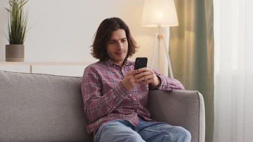 Young Man Using Smartphone Relaxing on Couch Indoors
