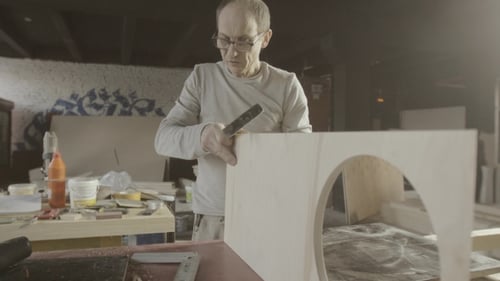 Man Using Hand Tool on Wood in Workshop