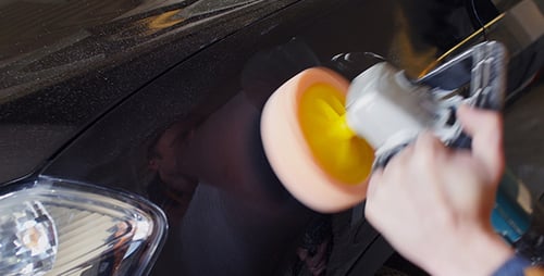 Man Polishing Scratches on Black Car with Tool