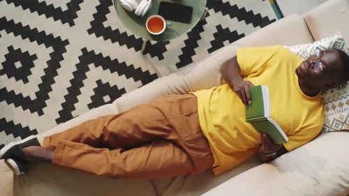 Man Relaxes Reading Book on Sofa at Home