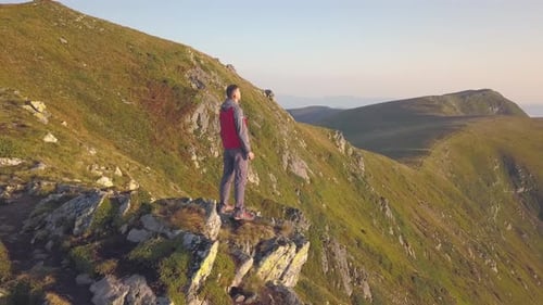 Hiker standing on top of rocky mountain enjoying magnificent view. Mountaineer looking at sunrise