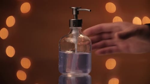 Handmodell, das einen transparenten Seifenspender vor einer wunderschönen Bokeh-Kulisse aufstellt.