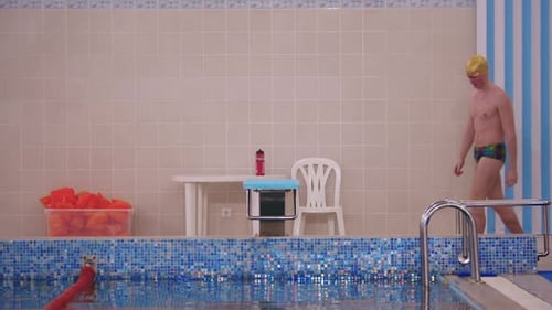 Fit Man Swimmer Walks to a Stand By the Pool and Stands Up on It
