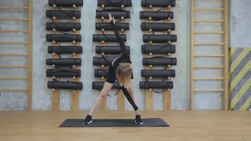 Young Athletic European Woman Doing A Stretching Exercise in the Gym, Dressed in Black Sportswear