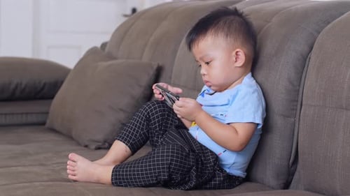 Child Plays on Smartphone on Couch at Home