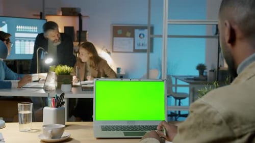 African American Office Worker Using Laptop with Chroma Key Green Screen in Workplace at Night