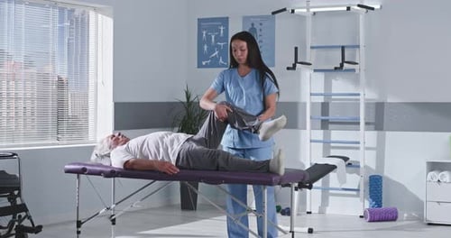 Rehabilitation Therapist Stretching Leg of Senior Patient