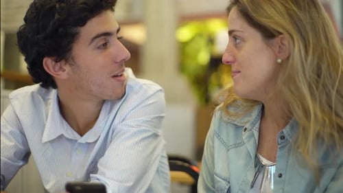 Friends Talking and Looking at Phone in Cafe