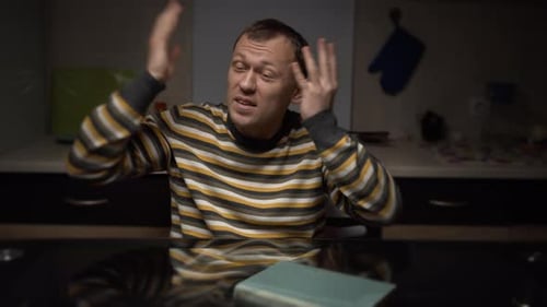 A man talks emotionally, gestures with his hands, sitting at home in the evening at home