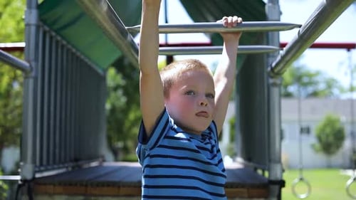Slow Motion shot of a young boy playing on the monkey bars on a playground set in his backyard.