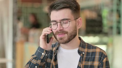 Porträt eines fröhlichen jungen Mannes, der auf dem Smartphone spricht