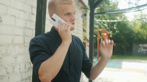 Cheerful Young Man Chatting on Mobile Phone Smiling Standing Outdoors in City on Summer Day
