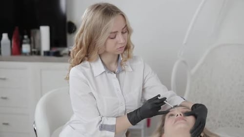 Manos de una cosmetóloga haciendo una inyección de Botox entre las cejas en la cara de una bella