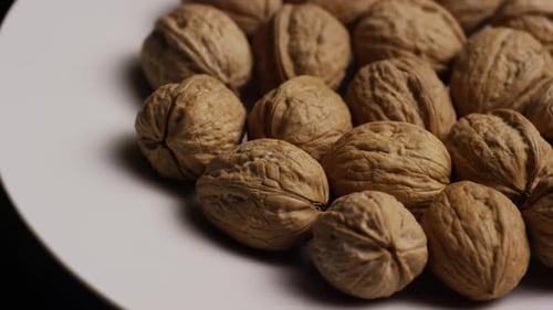 Filmmusik, rotierende Aufnahme von Walnüssen in ihren Schalen auf einer weißen Oberfläche - WALNUTS