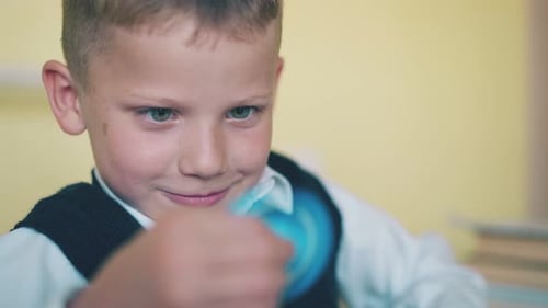 Un garçon heureux est assis à jouer avec un drôle de spinner bleu en classe