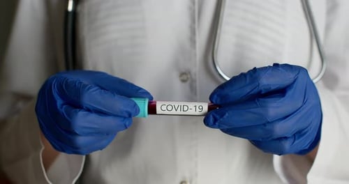 Close-up Shot. A Lab Worker in a Protective Suit Is Showing a Test Tube with the COVID-19