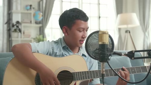 Chico vlogger asiático tocando la guitarra y cantando una canción. El niño está transmitiendo en vivo por Internet
