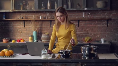 Woman Cooking While Using Laptop in Kitchen