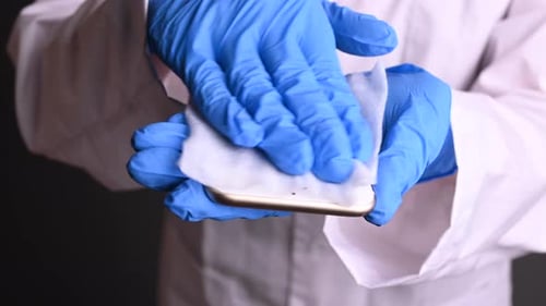 Hand with Gloves Disinfecting a Smartphone with Wipe