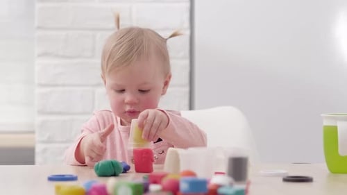 Toddler Girl Plays with Colorful Modeling Clay at Table