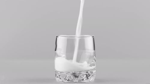 Milk Pouring Into Glass Close Up Isolated on Light Grey Background