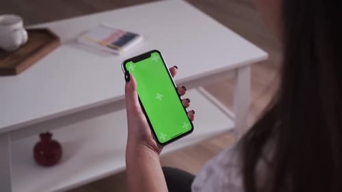 Home Isolated. Back View of Brunette Holding Chroma Key Green Screen Smartphone Watching Content
