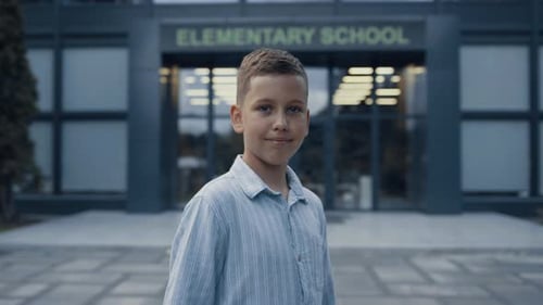 Niño sonriente de primaria de pie en la entrada de la escuela de cerca
