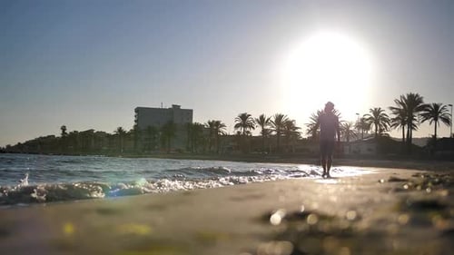 Silhouette of a young man in a hat and shorts walks along the beach during sunset